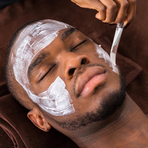 Therapist,Applying,Face,Mask,To,Young,African,Man,In,Spa