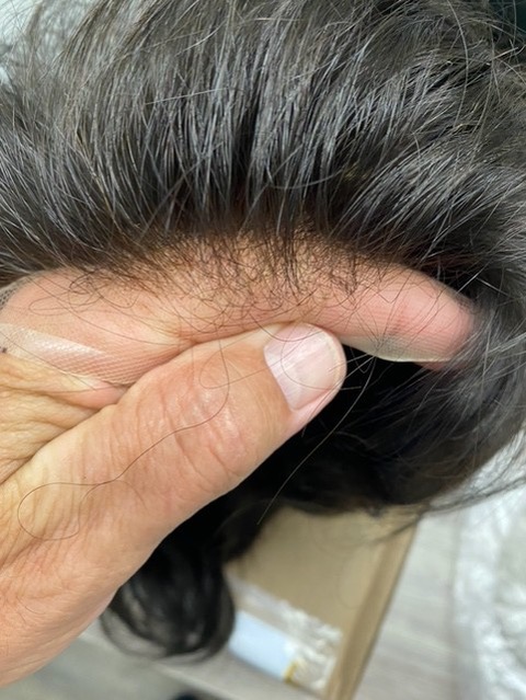 Close-up of a hand parting dark hair at the hairline.
