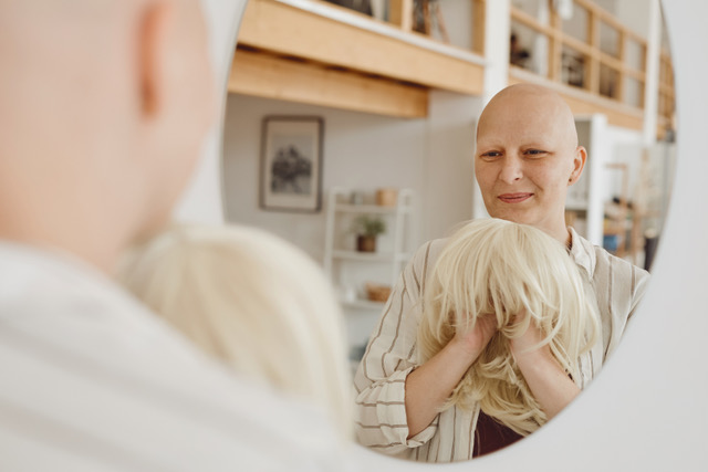 Person holding a blonde wig in front of a mirror.