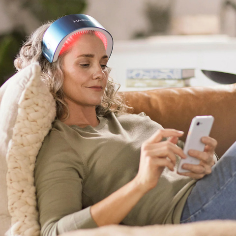 Person relaxing on a couch using a phone while wearing a light therapy head device.